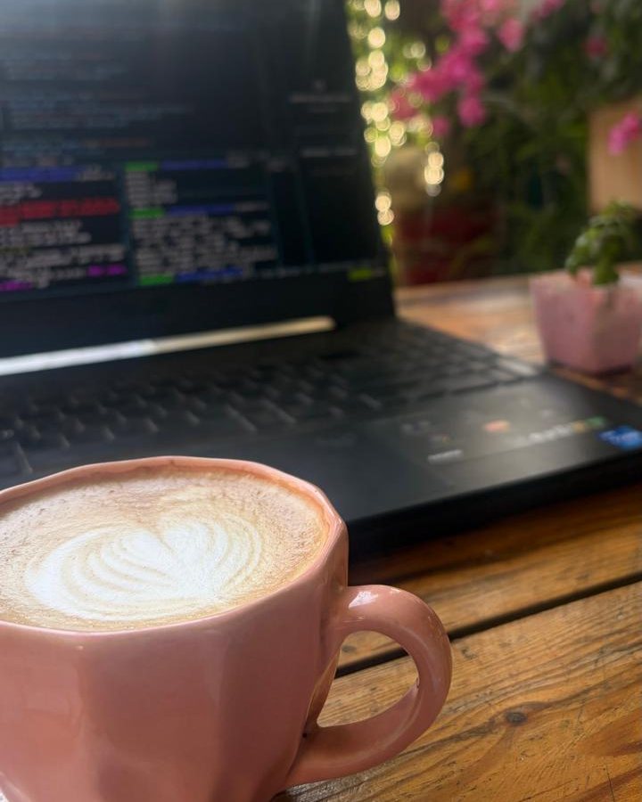 A latte beside a laptop with bougainvillea in the background