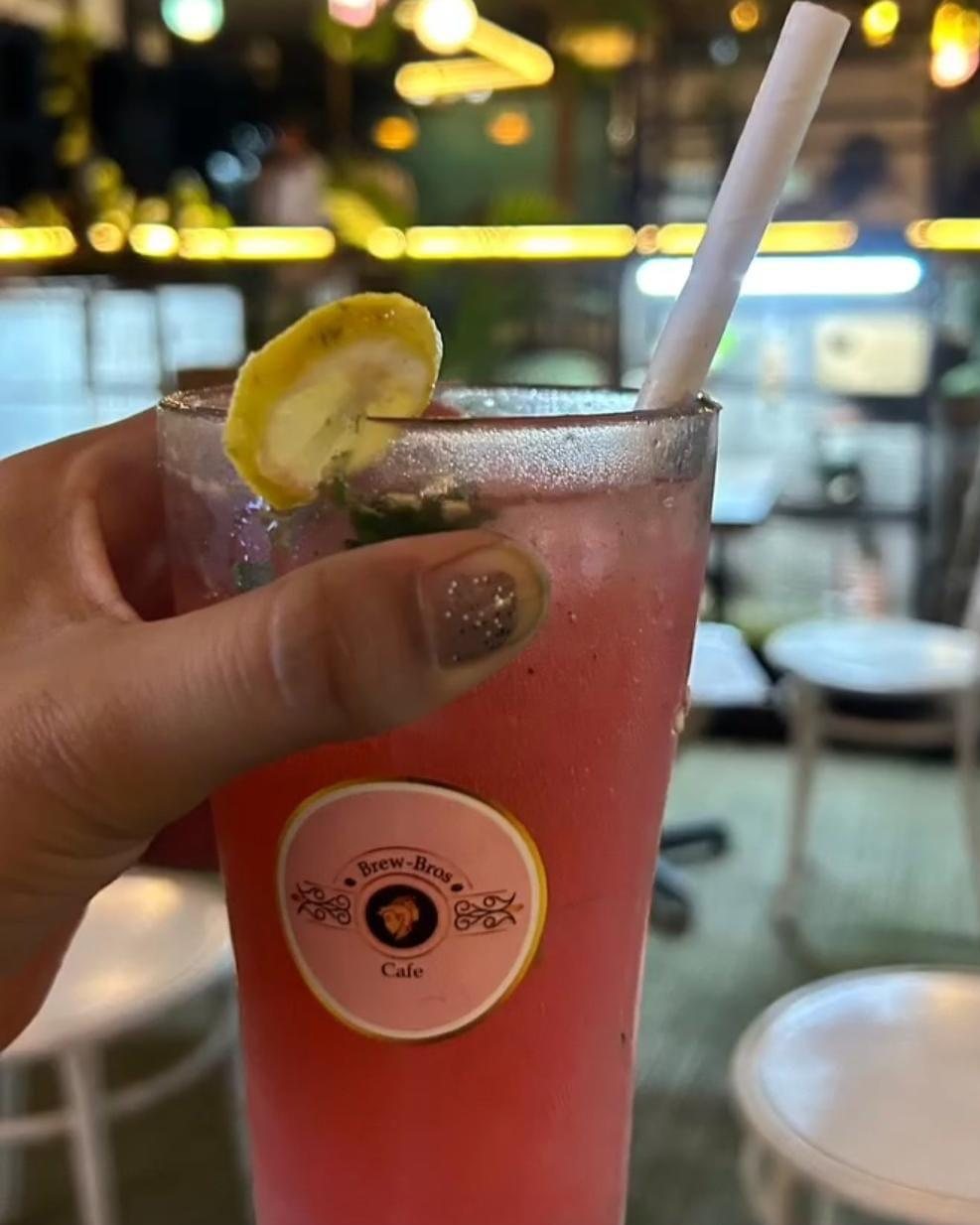 A hand holding a pink cooler in a glass with the Brew-Bros logo